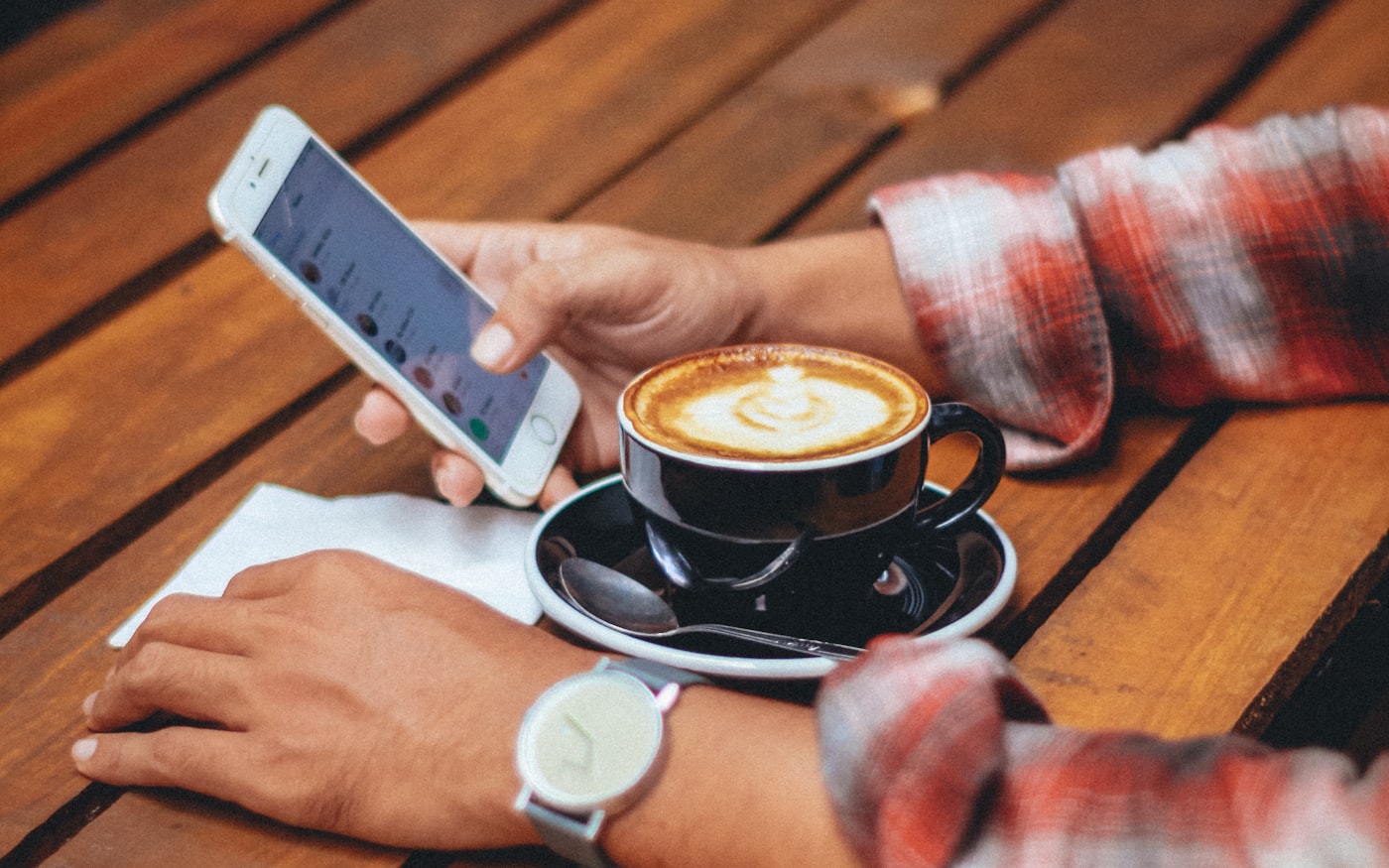 Hands holding a phone over a café table, coffee alongside